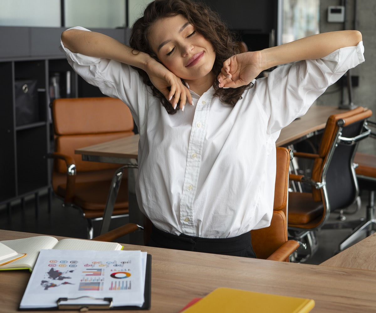 Une femme assise à un bureau, les bras levés, exprimant une attitude de joie ou d'enthousiasme.